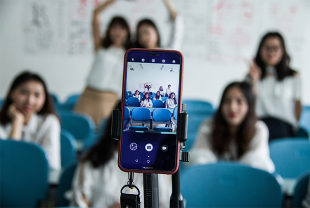 mobile phone in camera mode on tripod (in foreground) focused on classroom of teen girls posing for the camera
